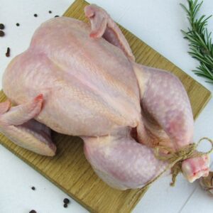 Overhead view of a raw, whole chicken with rosemary and spices on a wooden board.