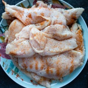 Close-up of raw chicken breasts seasoned, ready for cooking, on a decorative plate.